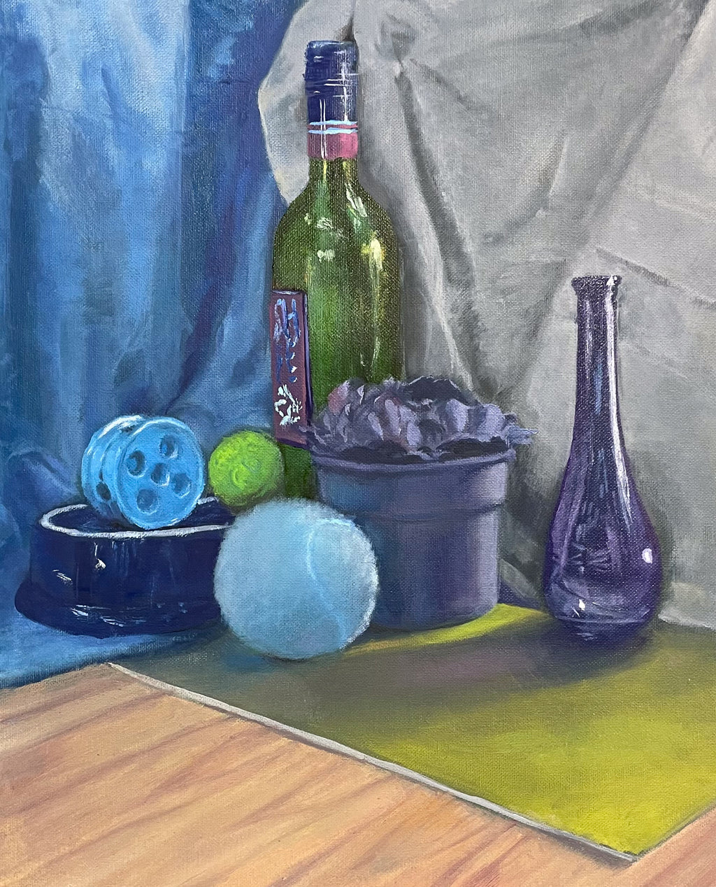 Still life oil painting featuring a green wine bottle, a blue glass vase, a blue ball, a light blue ball, a purple flower pot, and a blue tennis ball on a wooden tabletop against draped blue and gray fabric.